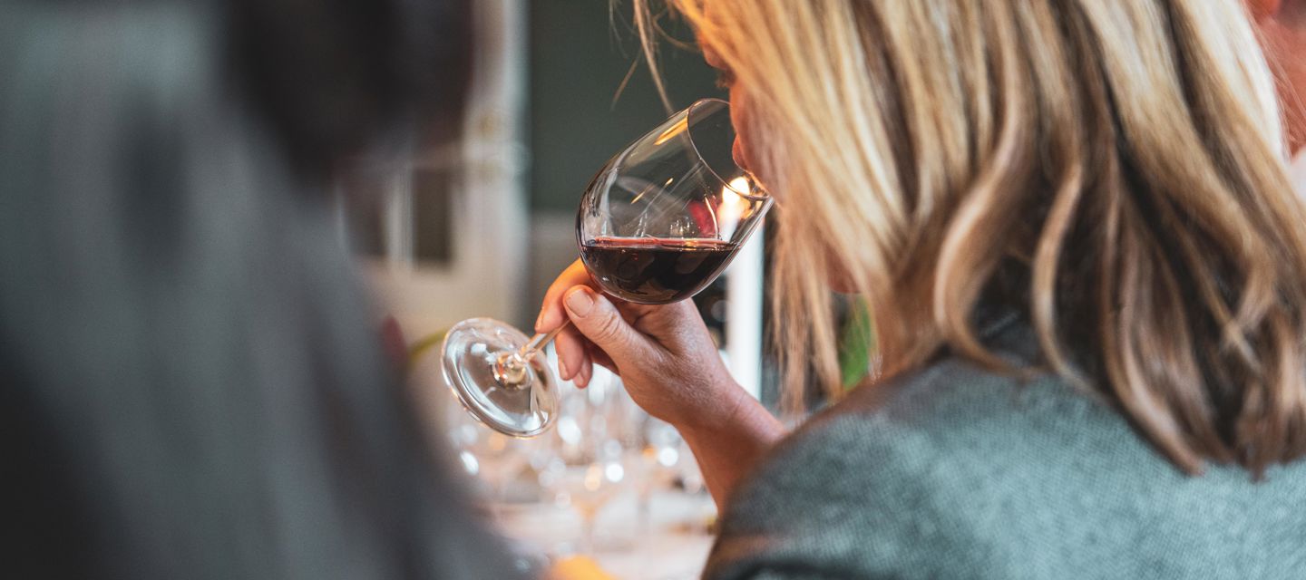 Kvinna doftar på ett upphällt rödvinsglas under en vinprovning